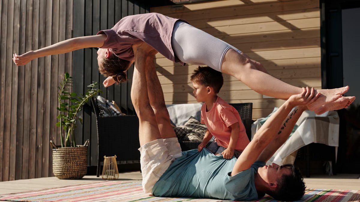 Father and kids doing yoga outdoors on a patio, balancing poses together.